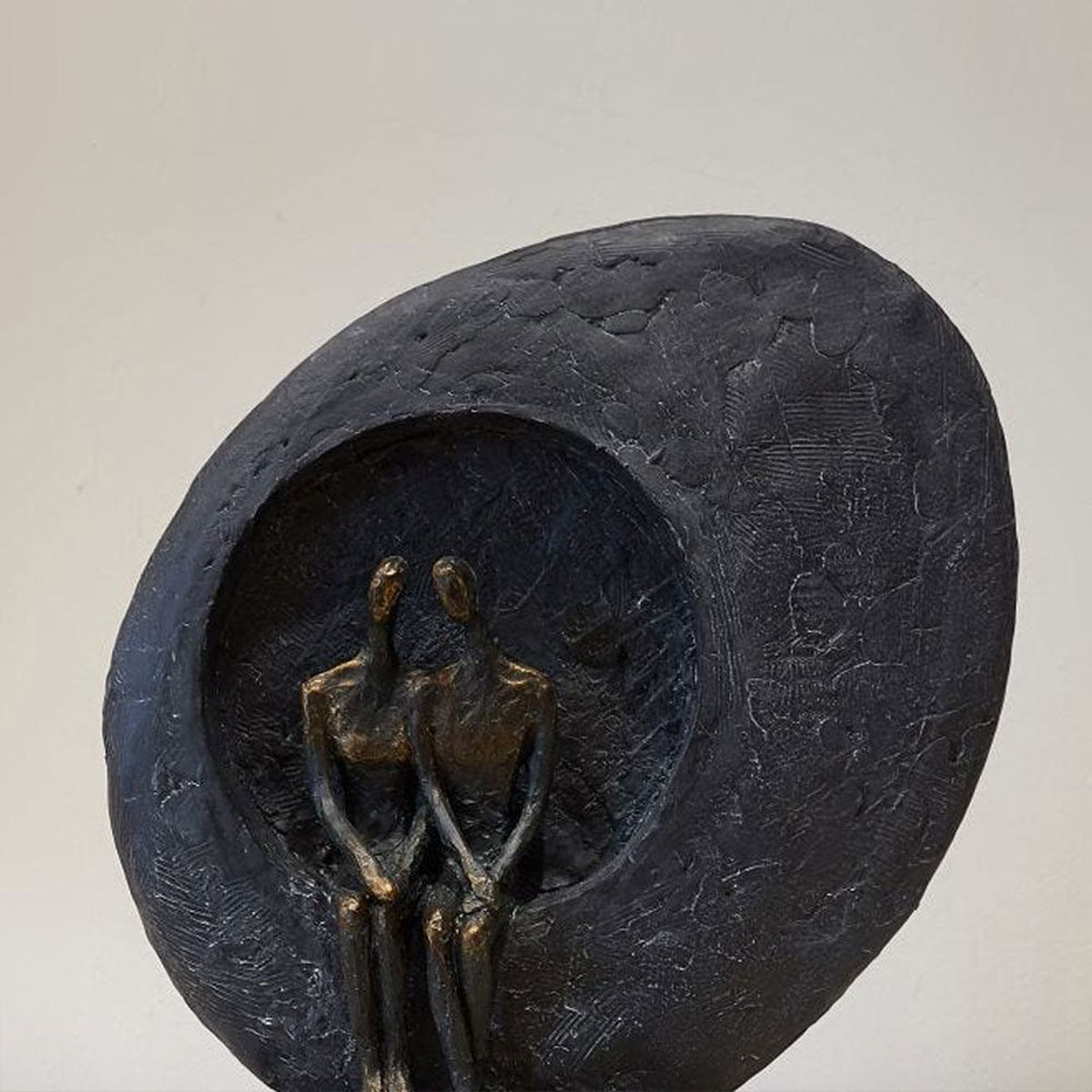 Bronze sculpture of two figures embracing inside a organic-shaped bowl on a light gray background