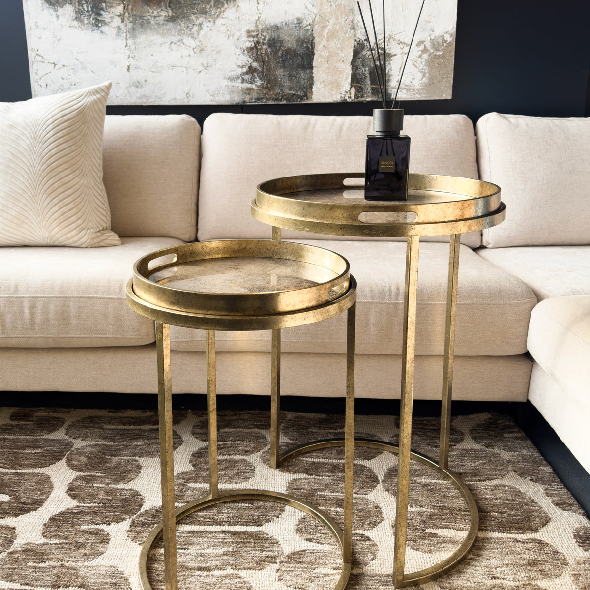 Gold nesting tables in a living room setting with a beige sofa and abstract art.