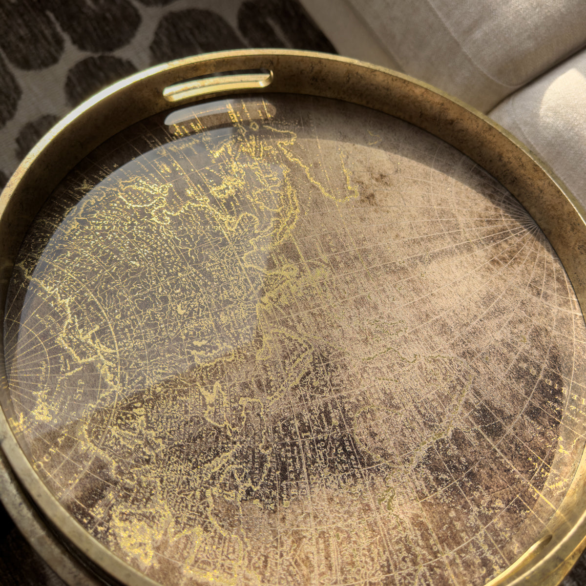 Round metal tray with engraved map design on a textured surface