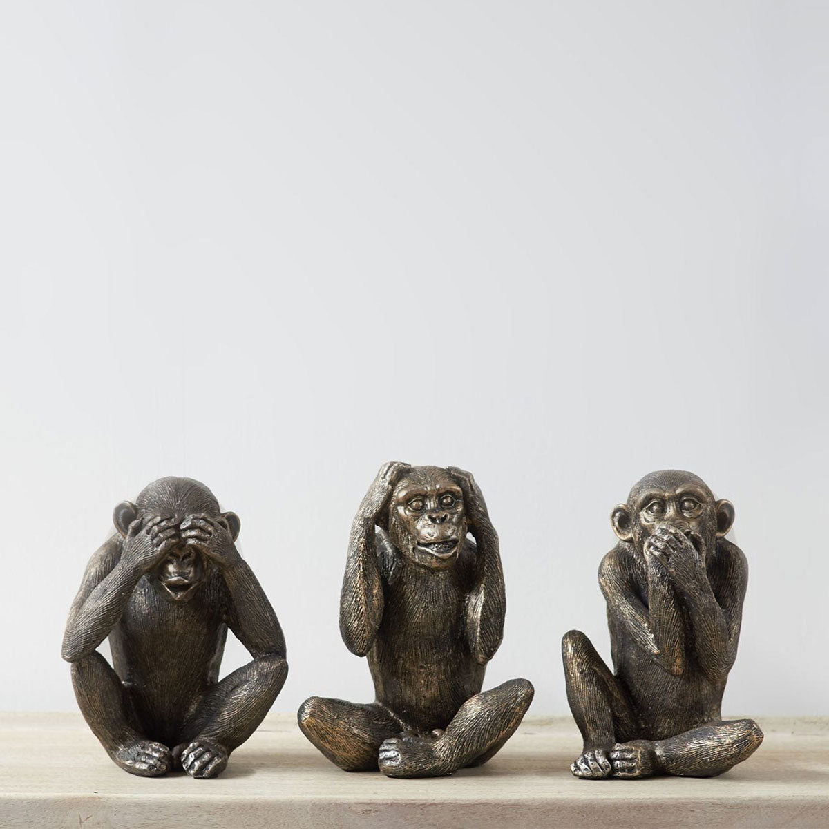 Three monkey statues representing 'see no evil, hear no evil, speak no evil' on a light surface with a white background.