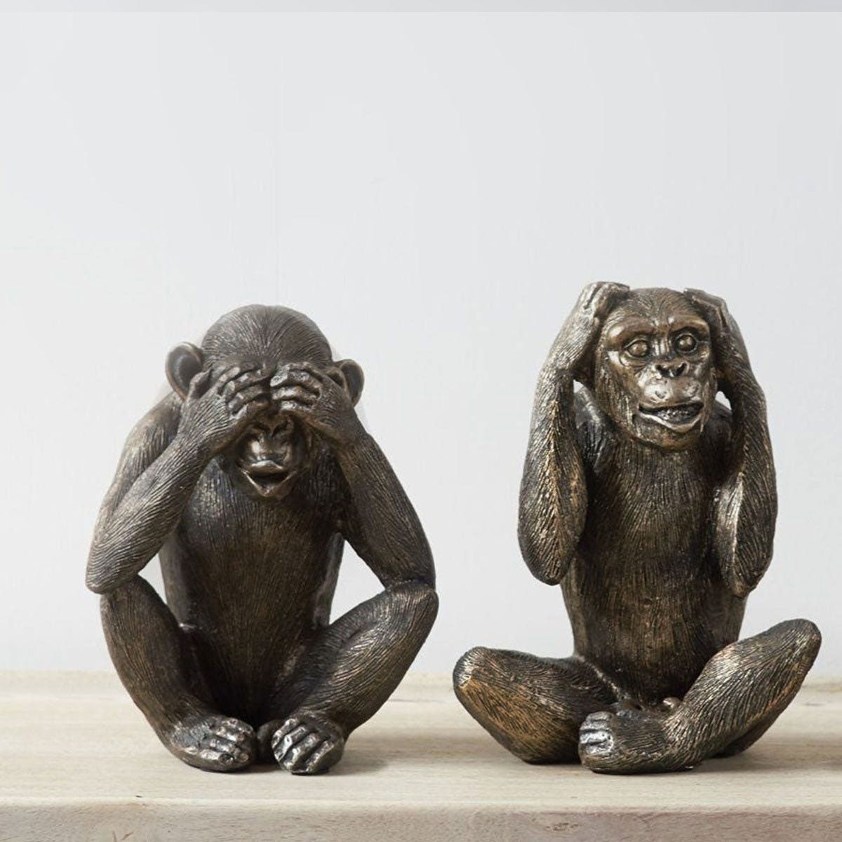 Two bronze monkey figurines on a light wooden surface with a plain background