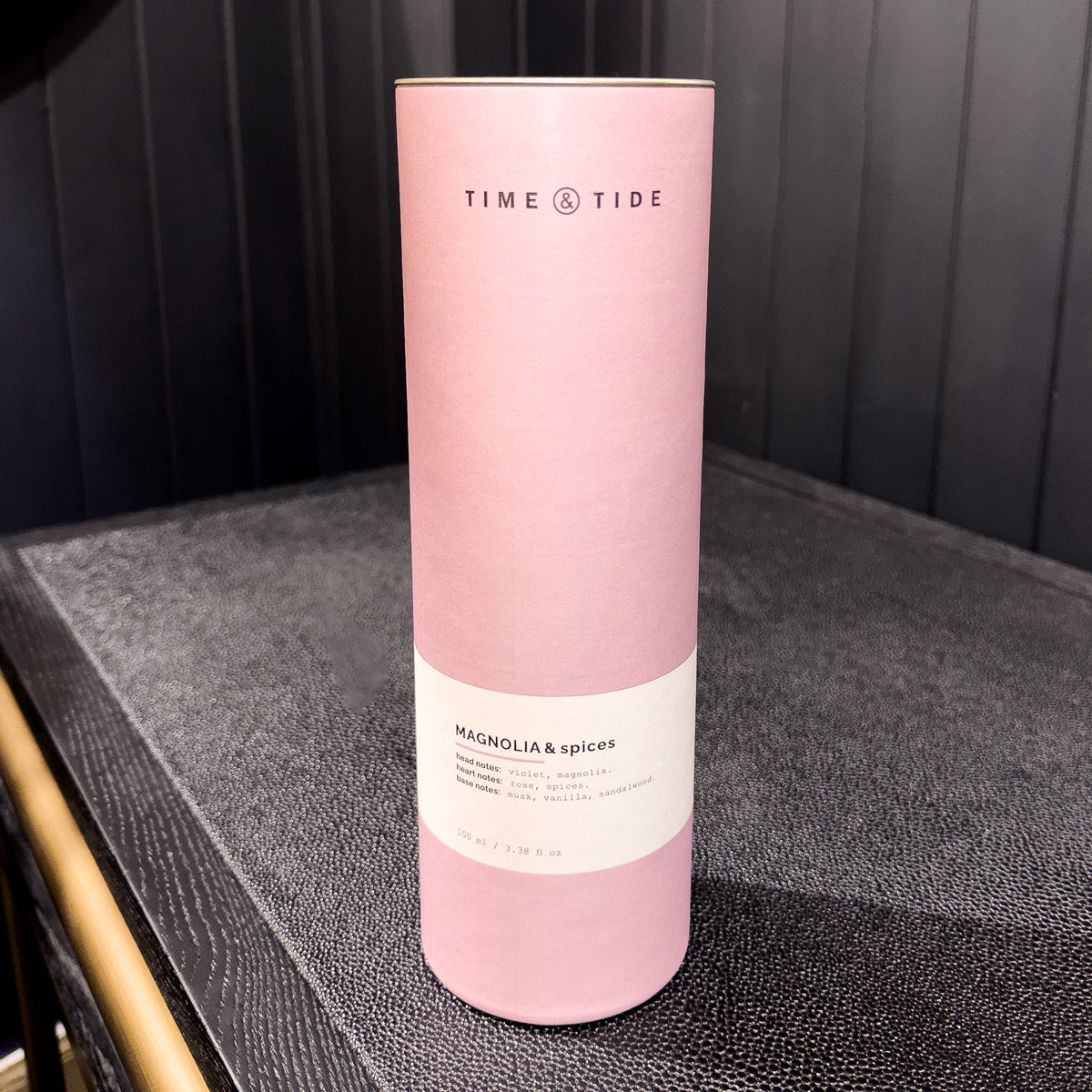 Pink cylindrical product packaging with 'Time & Tide' branding on a dark surface.