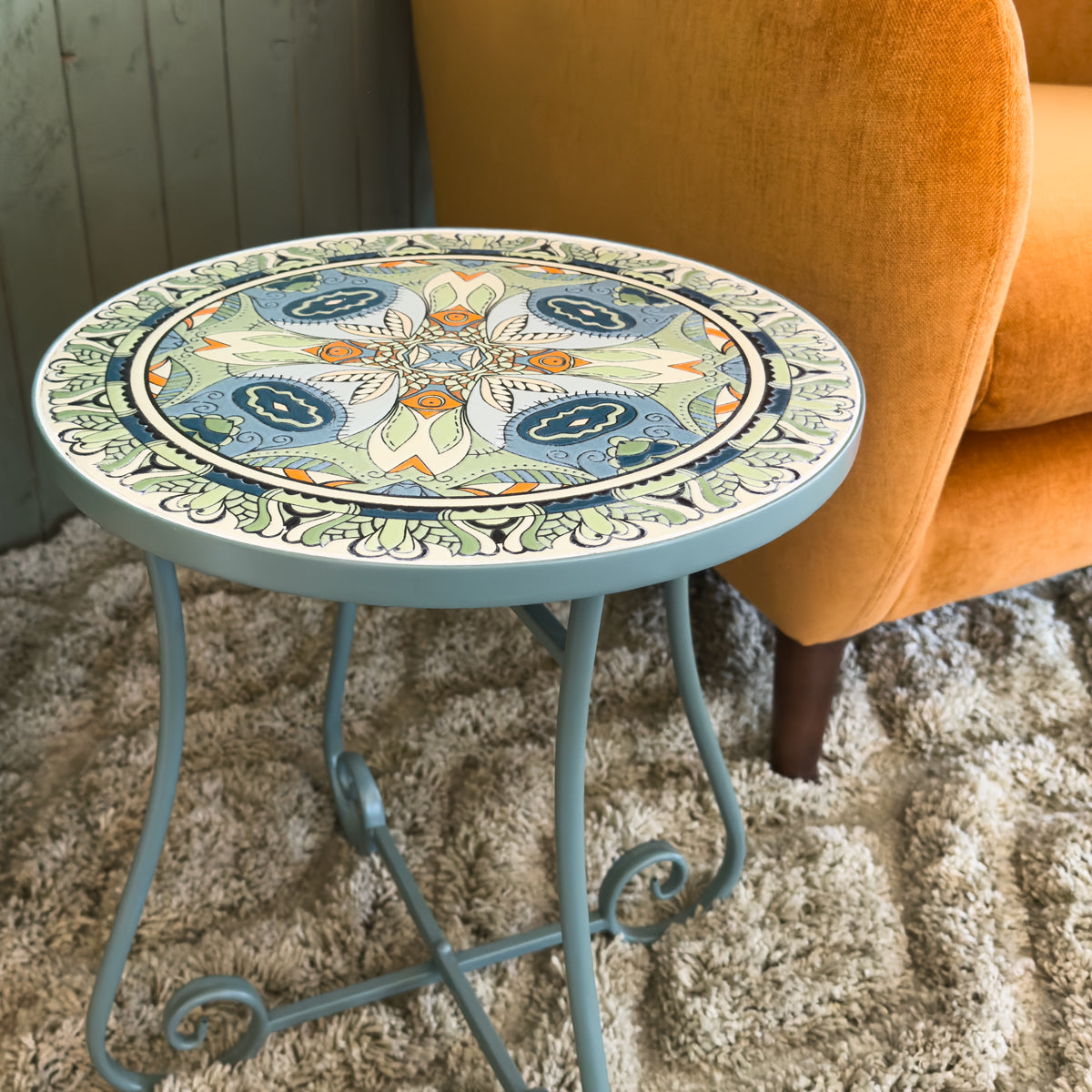 Decorative mosaic round table with intricate patterns next to an orange chair on a carpeted floor.