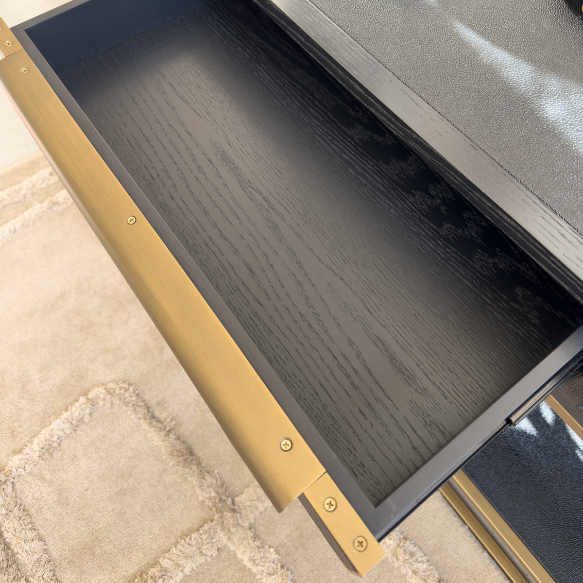 A close up of an open drawer, in black wood finish with a golden handle.