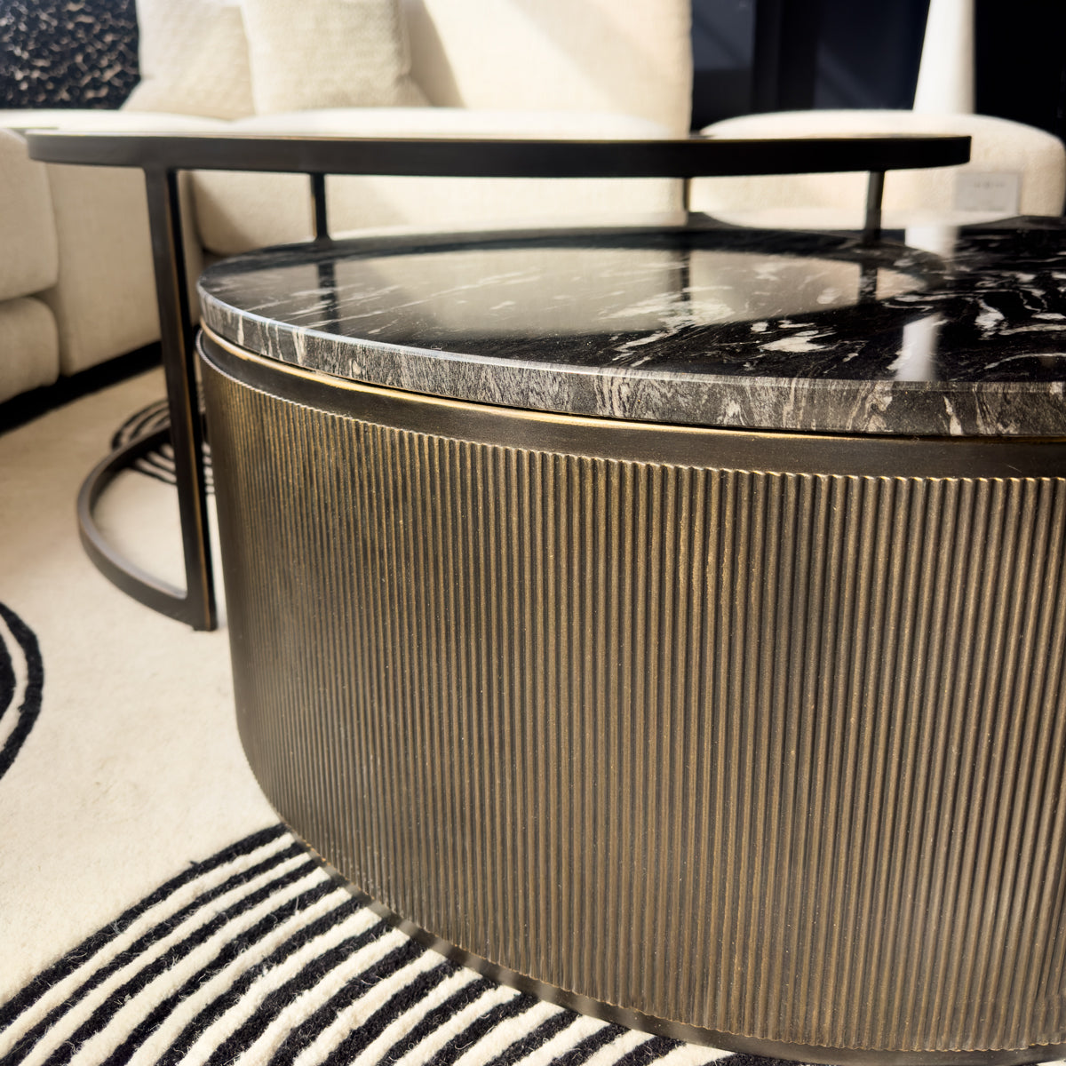Round coffee table with marble top and bronze base in a living room setting