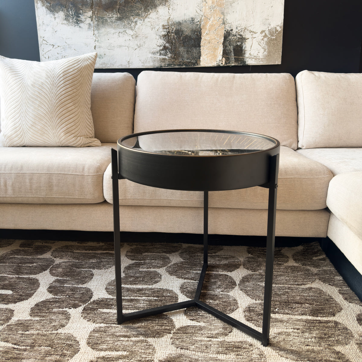 Modern black side table in front of a beige sectional sofa with a abstract painting in the background.