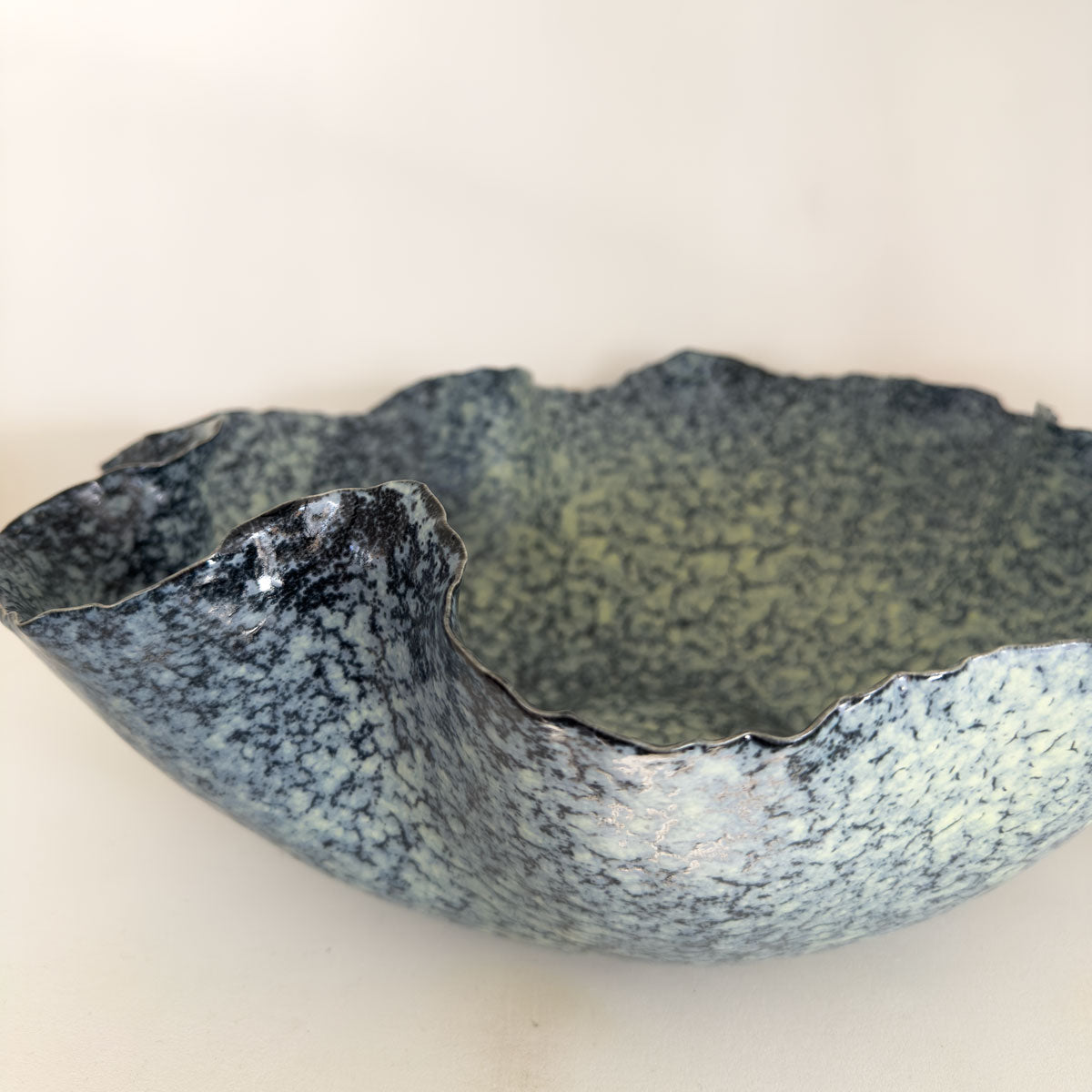 Speckled blue and green ceramic bowl on a beige background