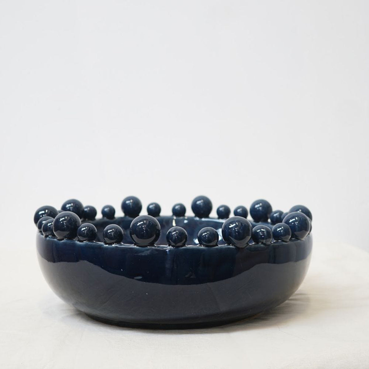 A navy blue bowl with bobble decorations around the rim, sitting against a white backdrop.