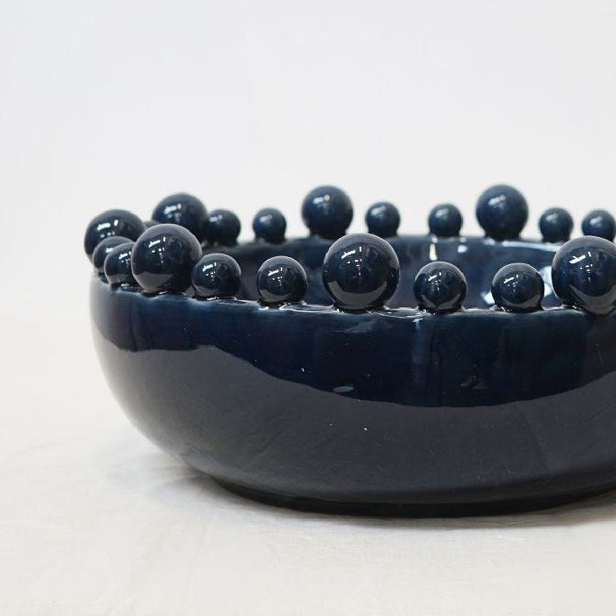 A navy blue ceramic decorative bowl, sitting against a white backdrop.