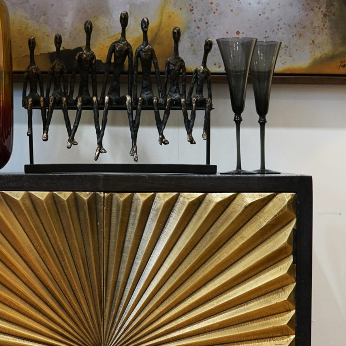 Decorative objects including a sculpture of bronze figures and two tall black glasses on a cabinet with textured gold doors