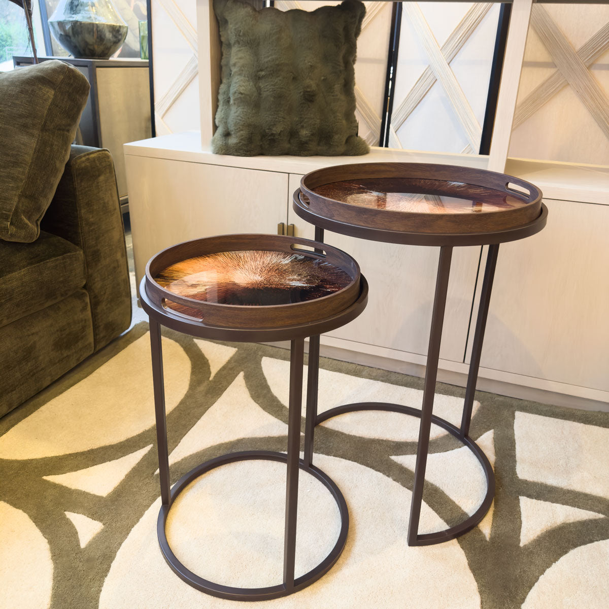 Two round tray tables in a living room setting with a couch and decorative green cushions.