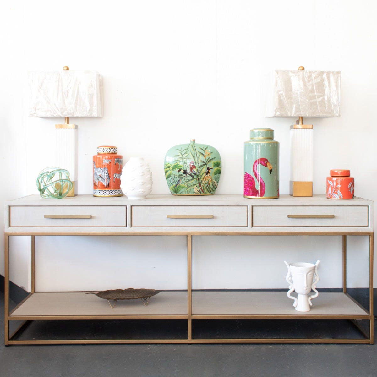A cream parquet console table with two lamps and colourful vases on top