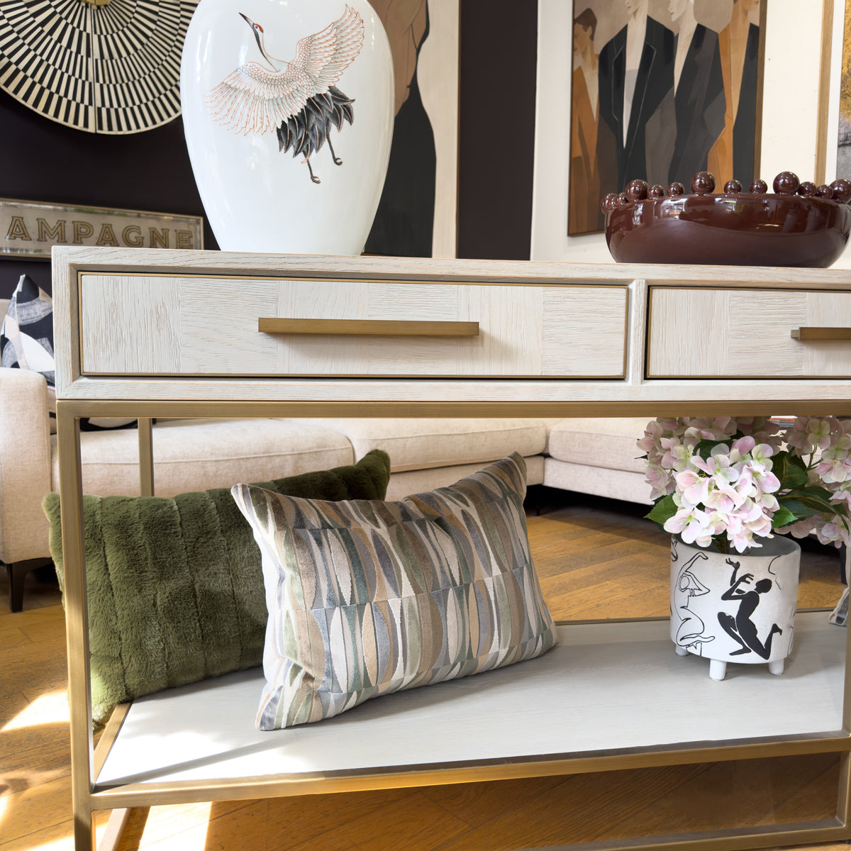 A parquet console table with a light wood top, gold metal frame and drawers, styled in a living room setting