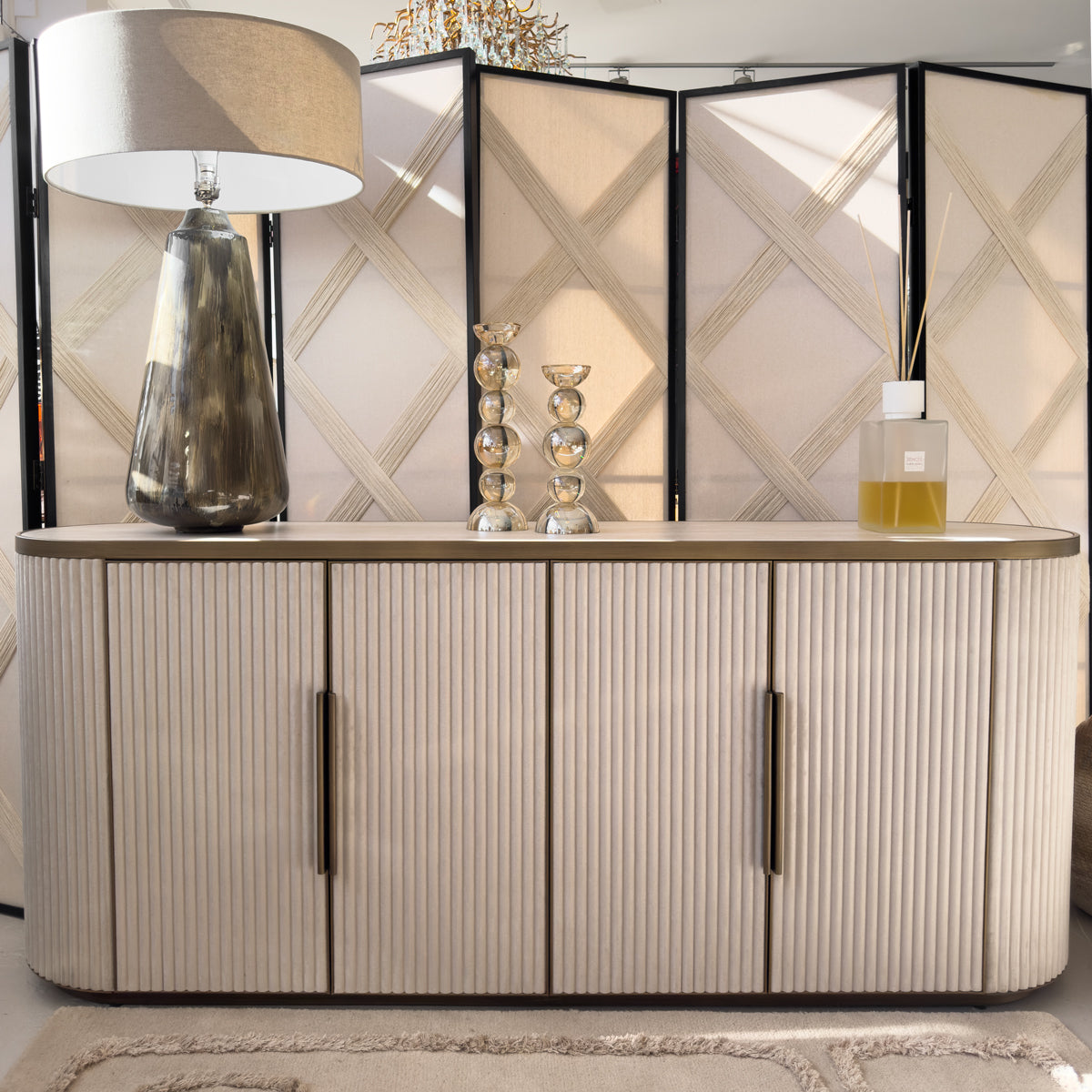 A cream coloured velvet sideboard with gold hardware, sitting infront of woven room dividers.
