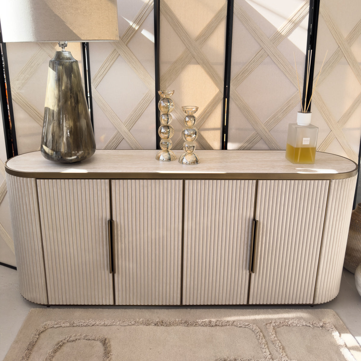 A neutral velvet sideboard with a table lamp, two bubbled glass candleholders and a diffuser on top.