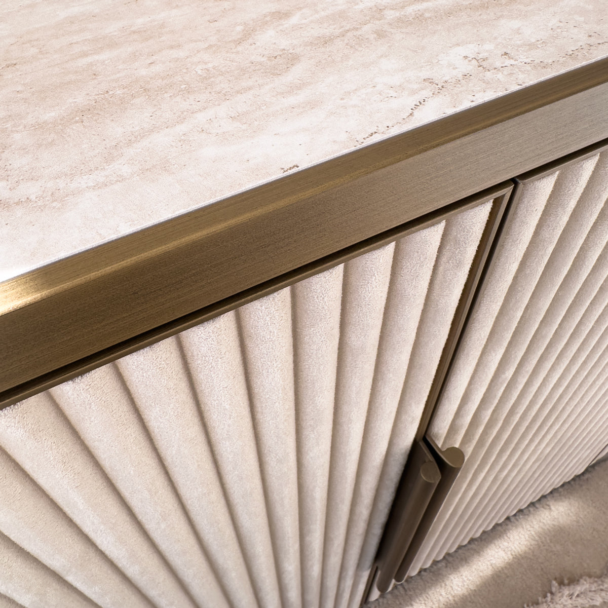A close up of a cream velvet sideboard, with ridged doors and golden trims and handles.