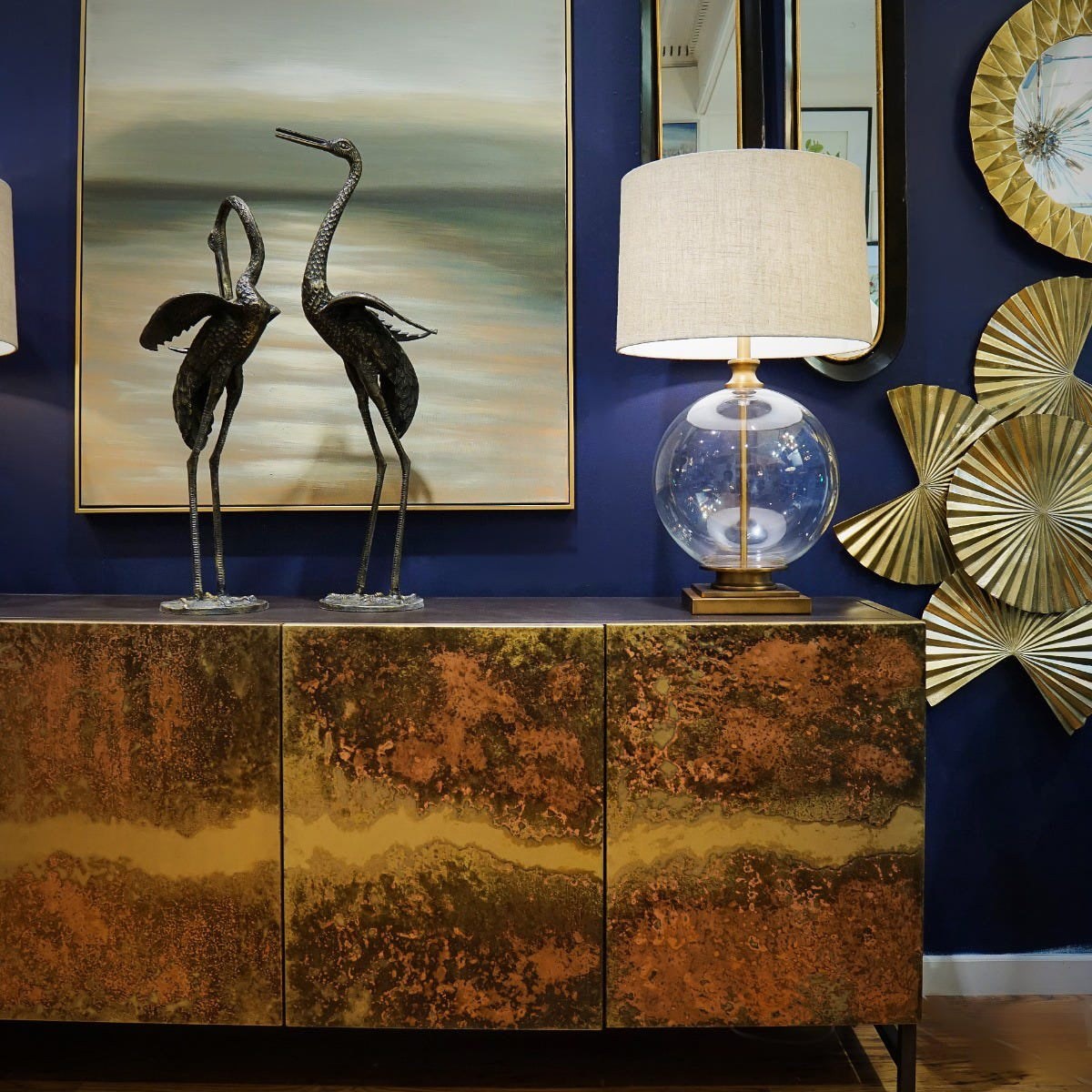 Decorative interior setting with a bronze cabinet, lamp, and wall art.