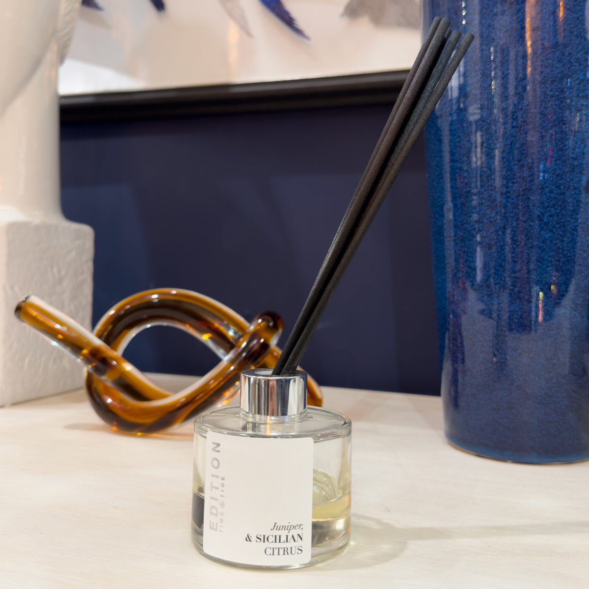 Diffuser with black reeds on a surface with decorative items in the background