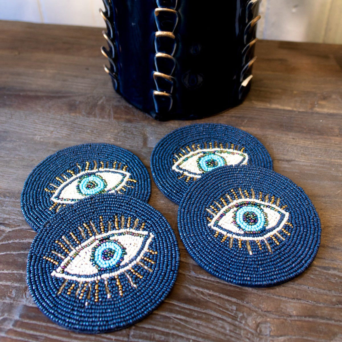 Set of four blue beaded coasters with eye design on a wooden surface.