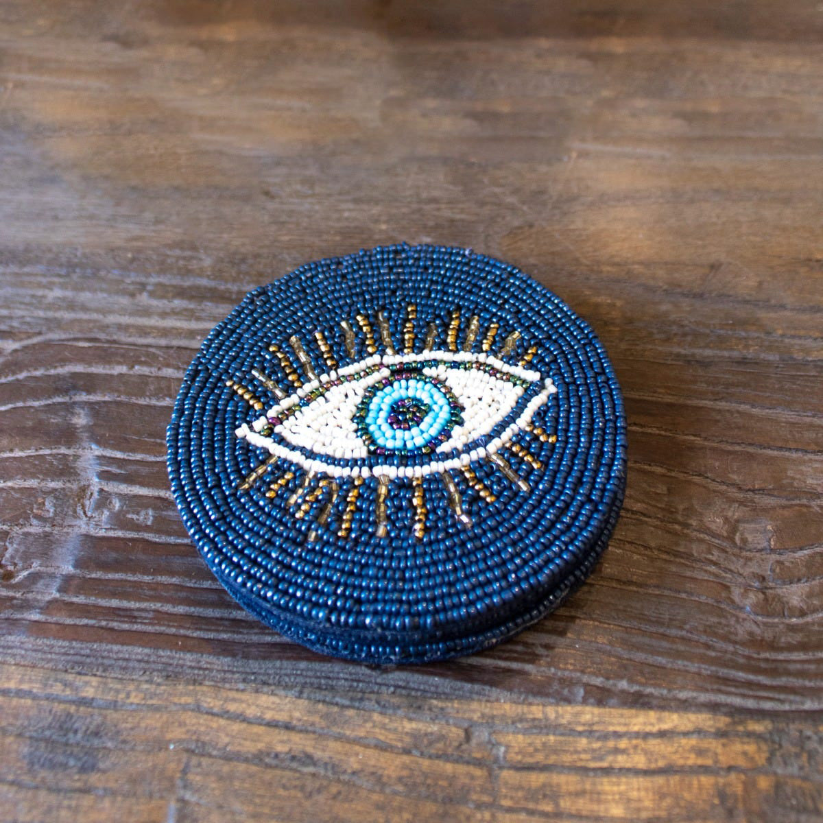 Beaded eye design on a round blue coasters on a wooden surface