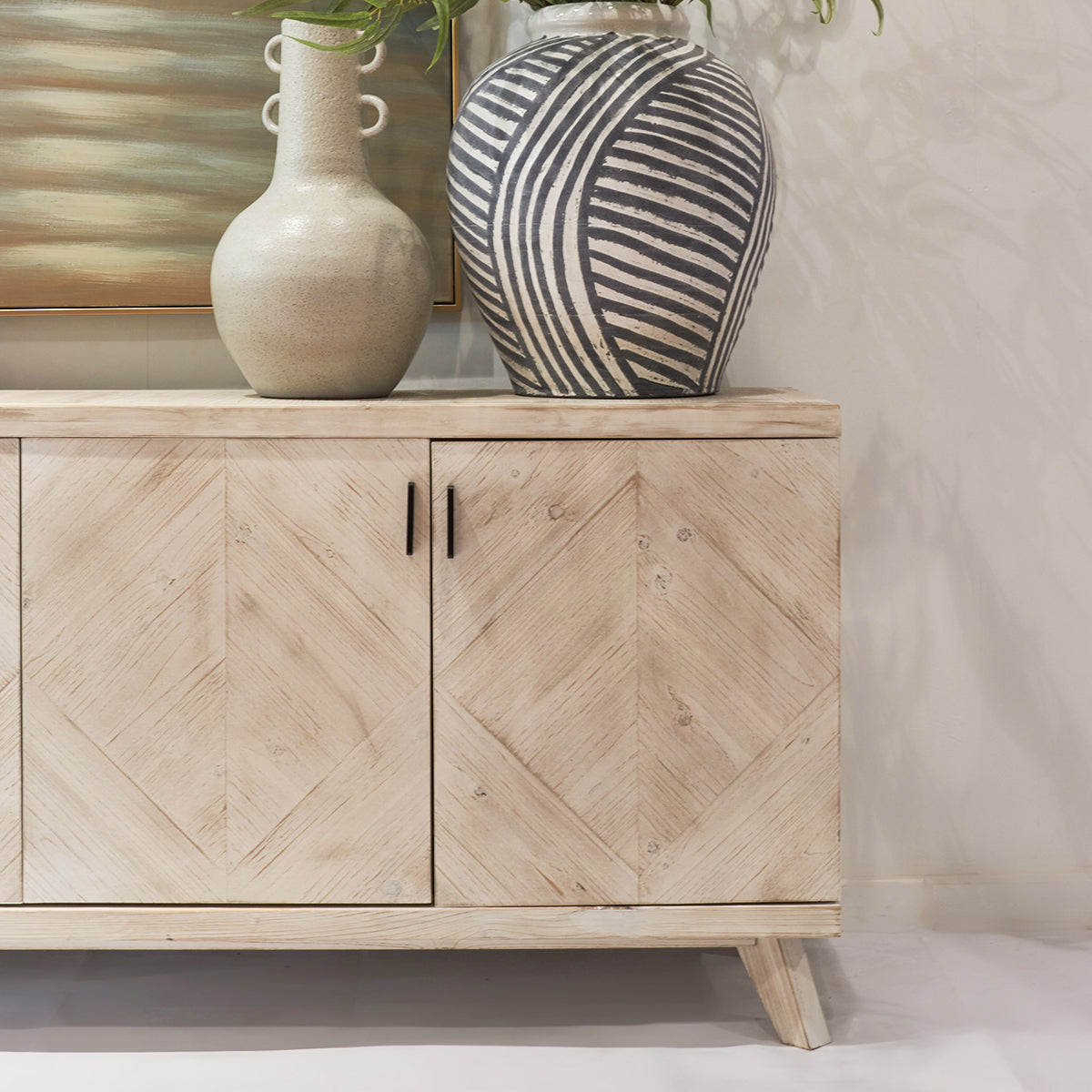 Wooden cabinet with two doors, featuring a herringbone pattern, against a neutral wall with decorative vases on top.