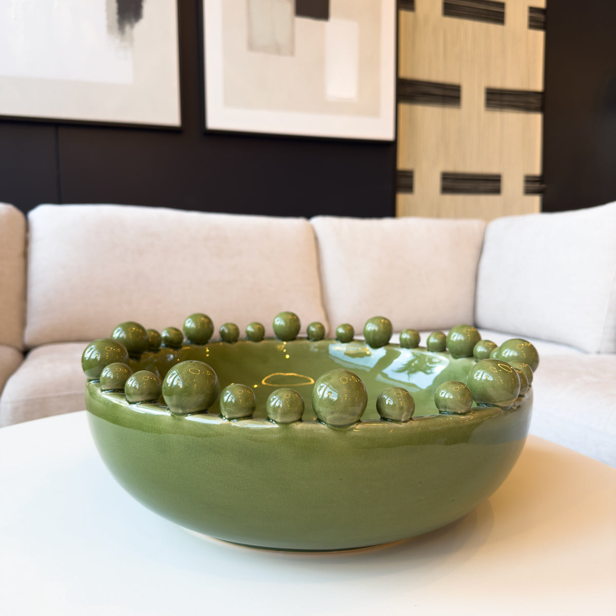 A decorative green bobble bowl sitting on top of a white coffee table, in a living room setting.