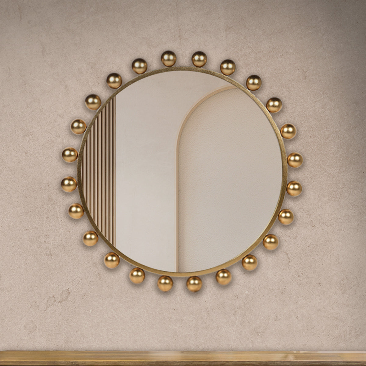 A gold bobble round mirror hanging on a neutral concrete wall.