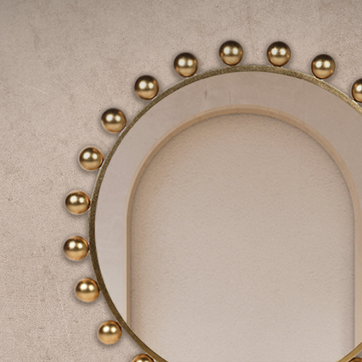 A close up of a gold ball surround mirror hanging on a beige concrete wall.
