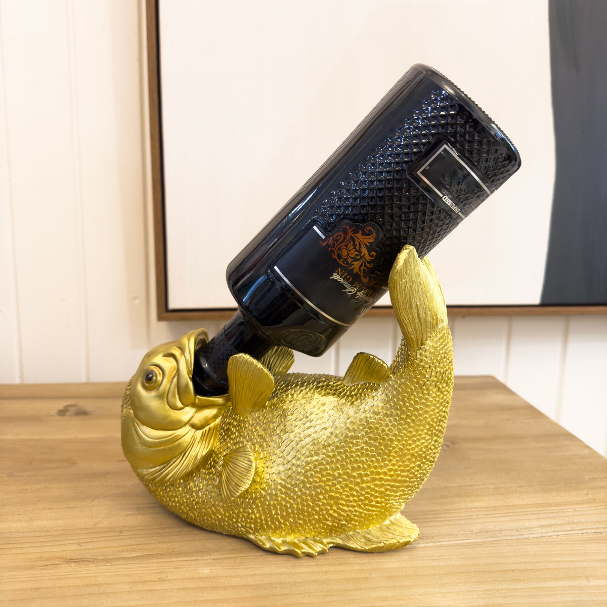Gold fish-shaped bottle holder with a wine bottle on a wooden surface.
