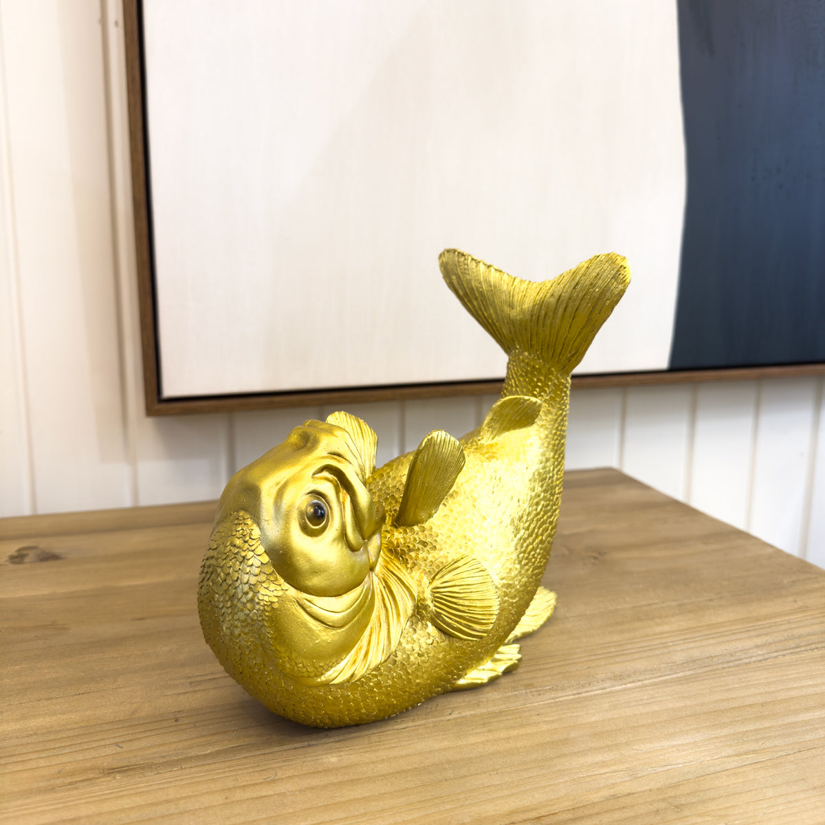 Gold fish sculpture on a wooden surface with a neutral background