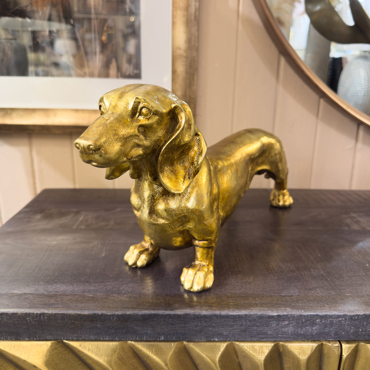 Gold sausage dog statue on a dark surface with a mirror in the background