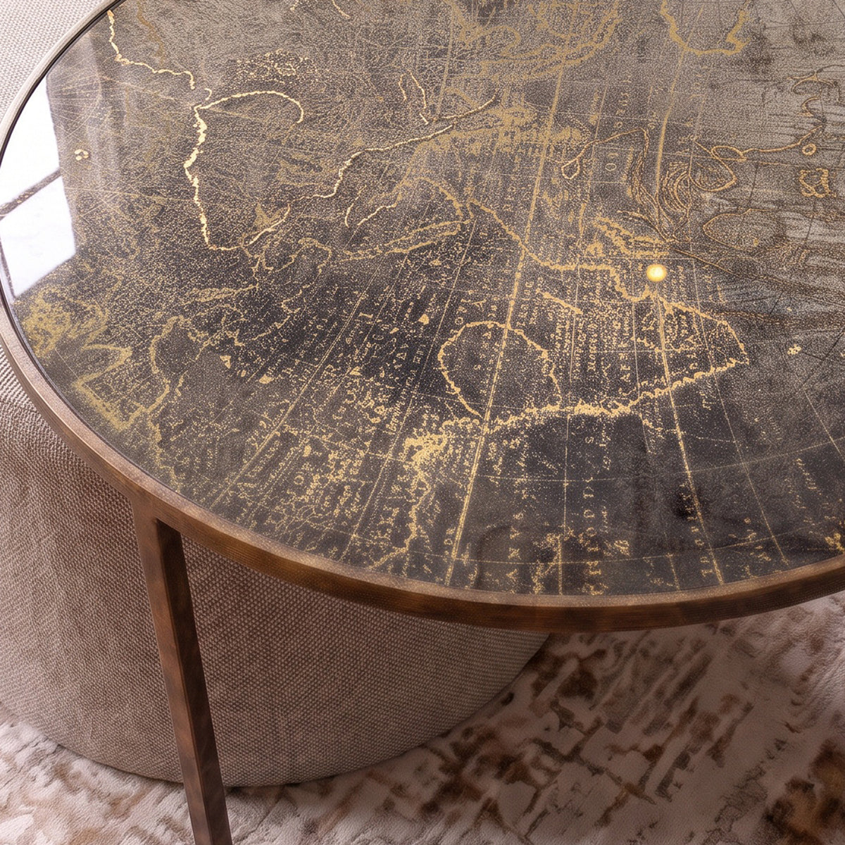A close-up of a round coffee table with a distressed antique-style world map glass top and a gold metal frame, paired with a textured beige cylindrical side stool.