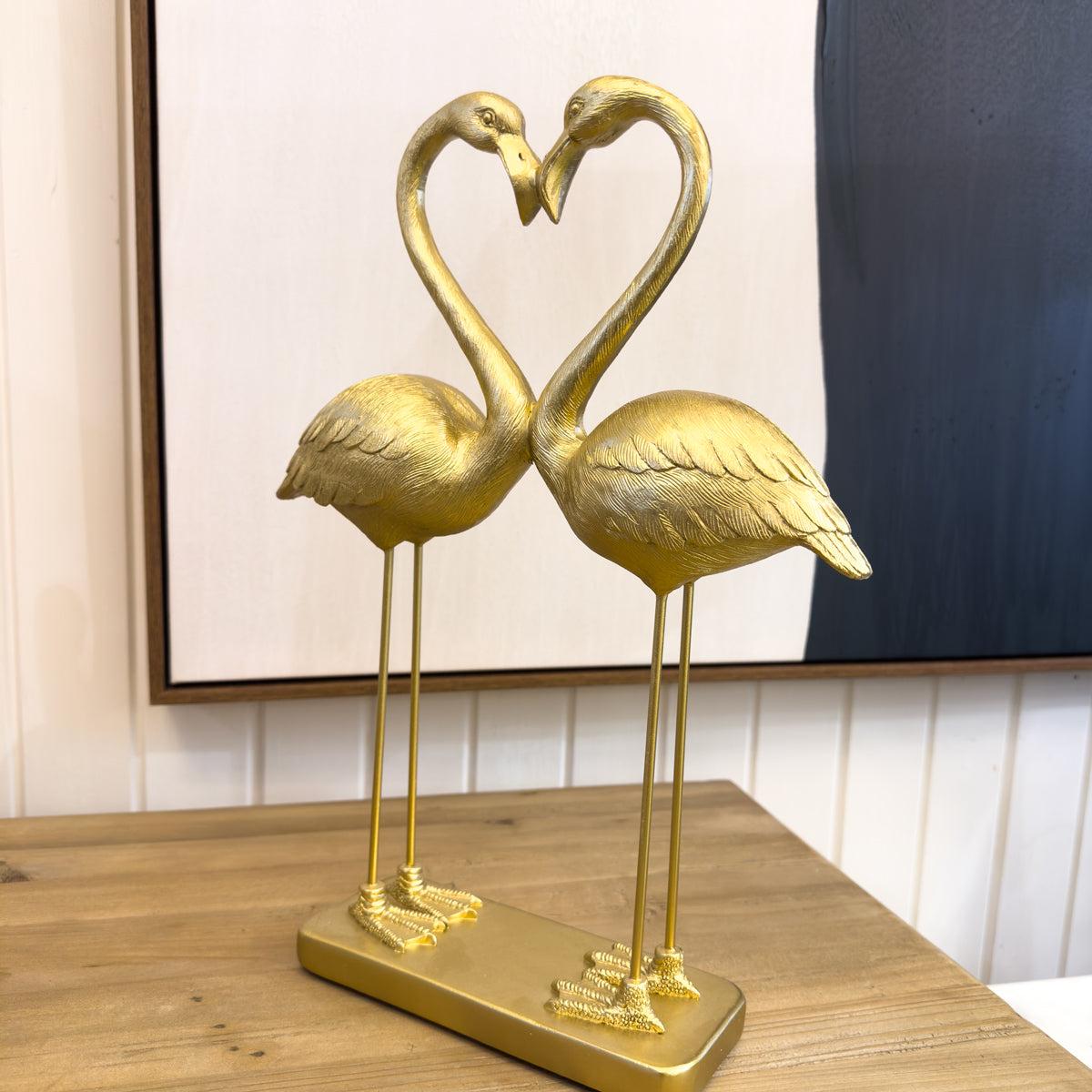 Gold flamingo sculpture forming a heart shape on a wooden surface.