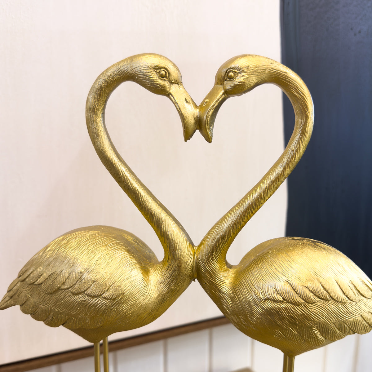 Gold flamingo sculpture forming a heart shape against a neutral background