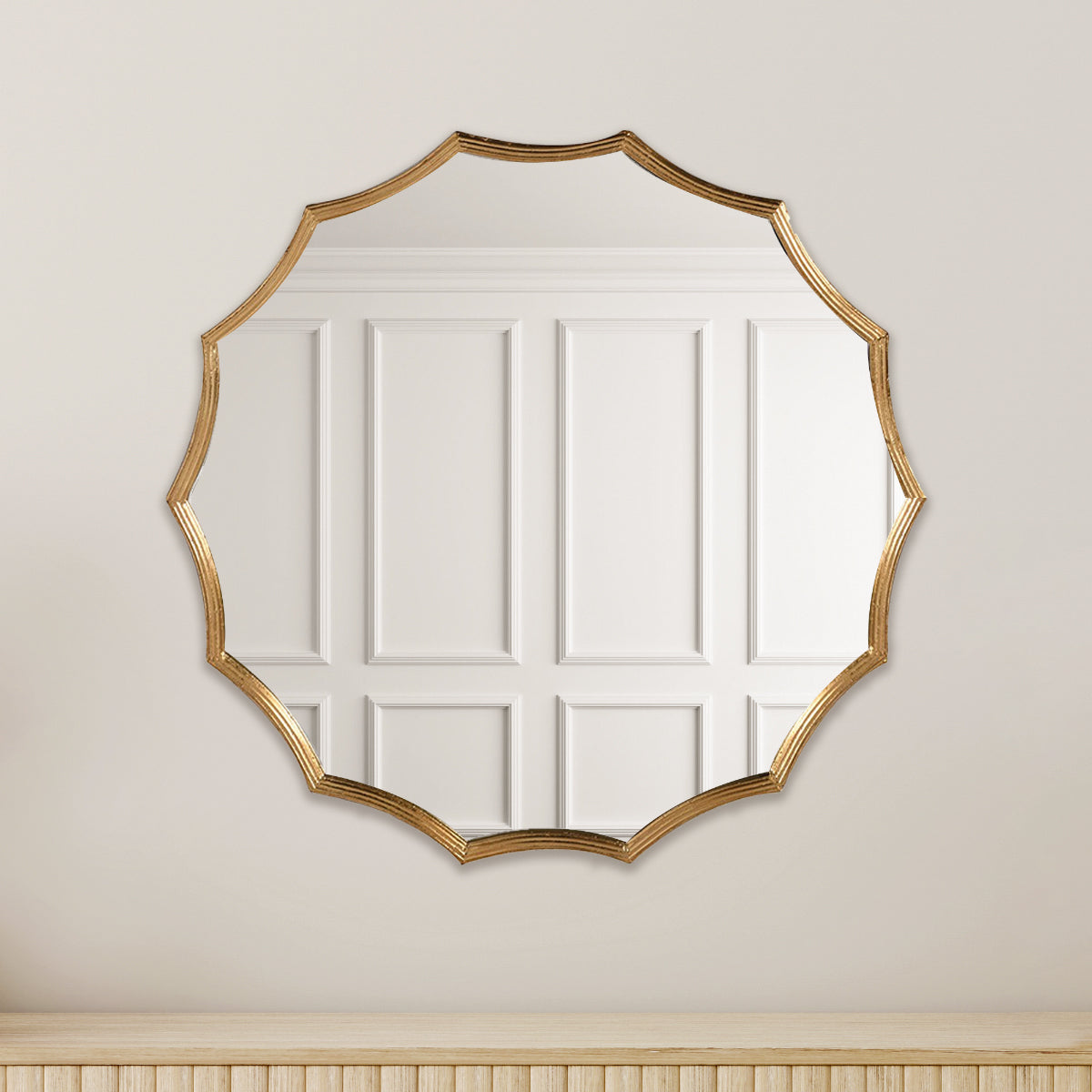 A golden scalloped edge wall mirror hannging above a natural ridged wood sideboard.