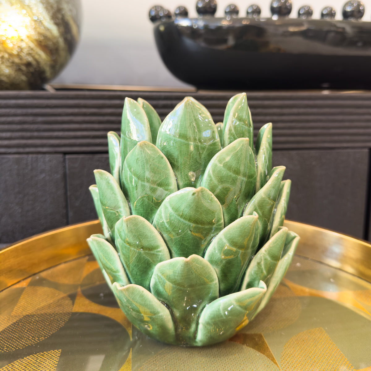 Glazed ceramic tealight holder resembling an artichoke with green petals, sitting on a gold surface.