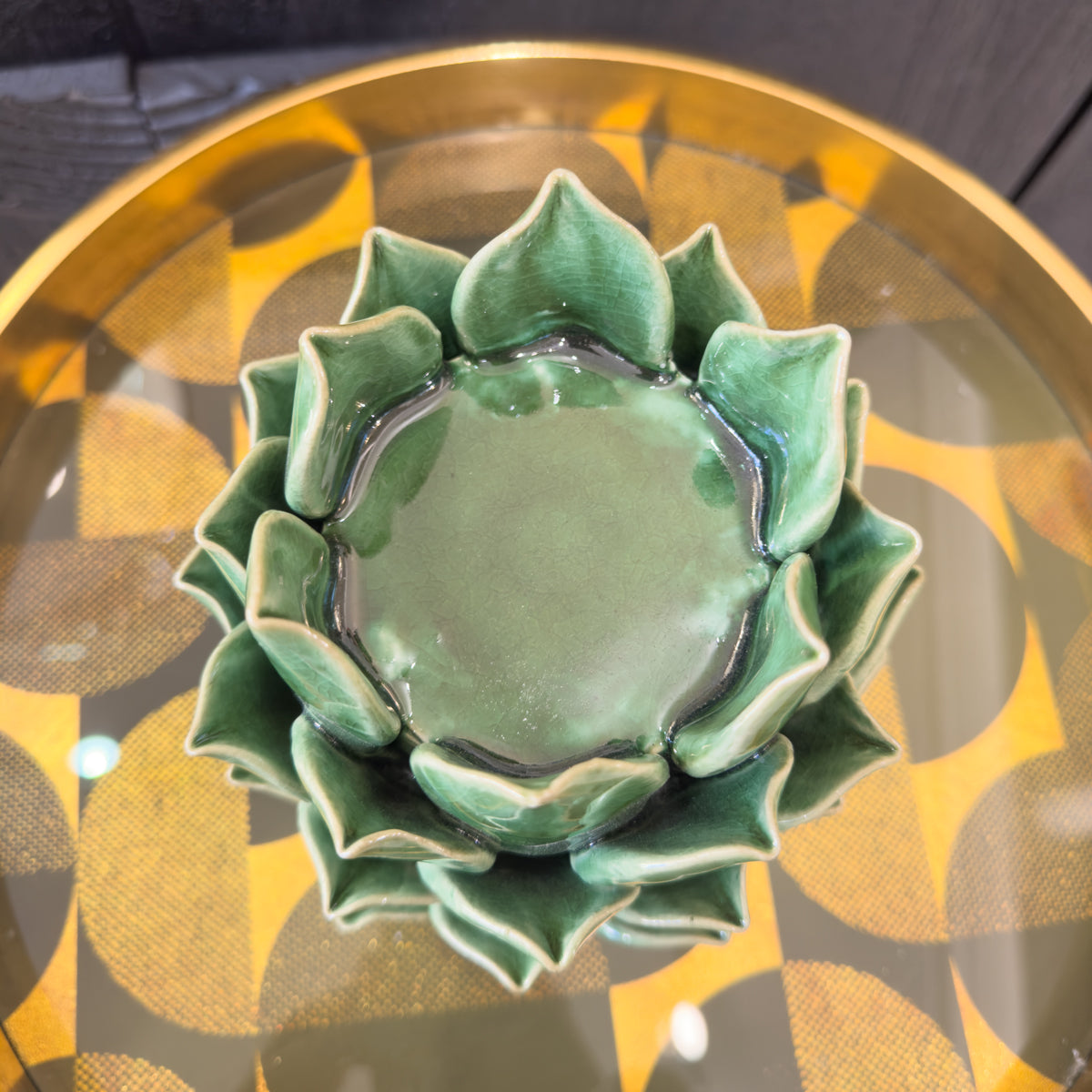 Green ceramic flower-shaped candleholder on a reflective surface with a gold rim