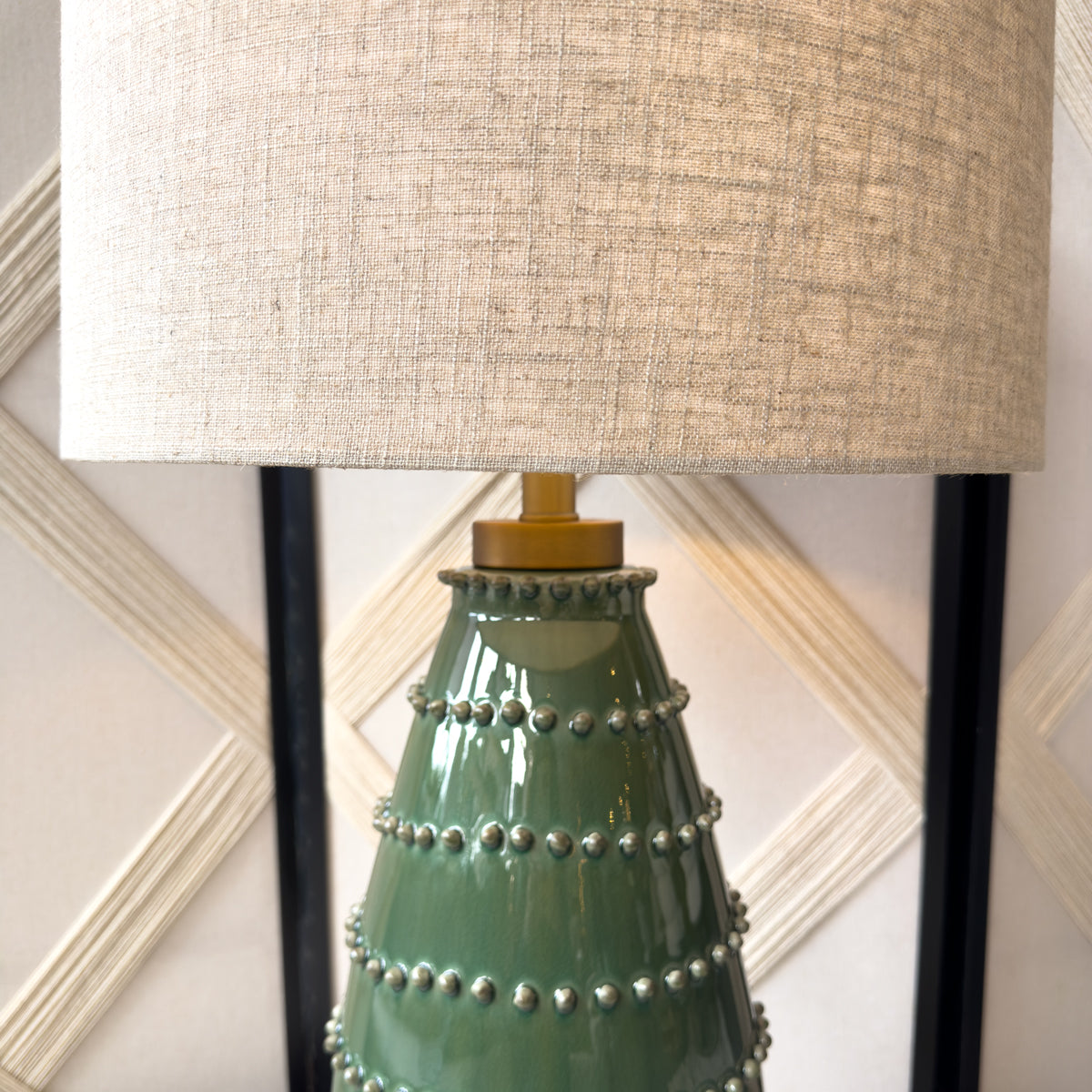 A green table lamp with ceramic bobbles and a beige linen shade