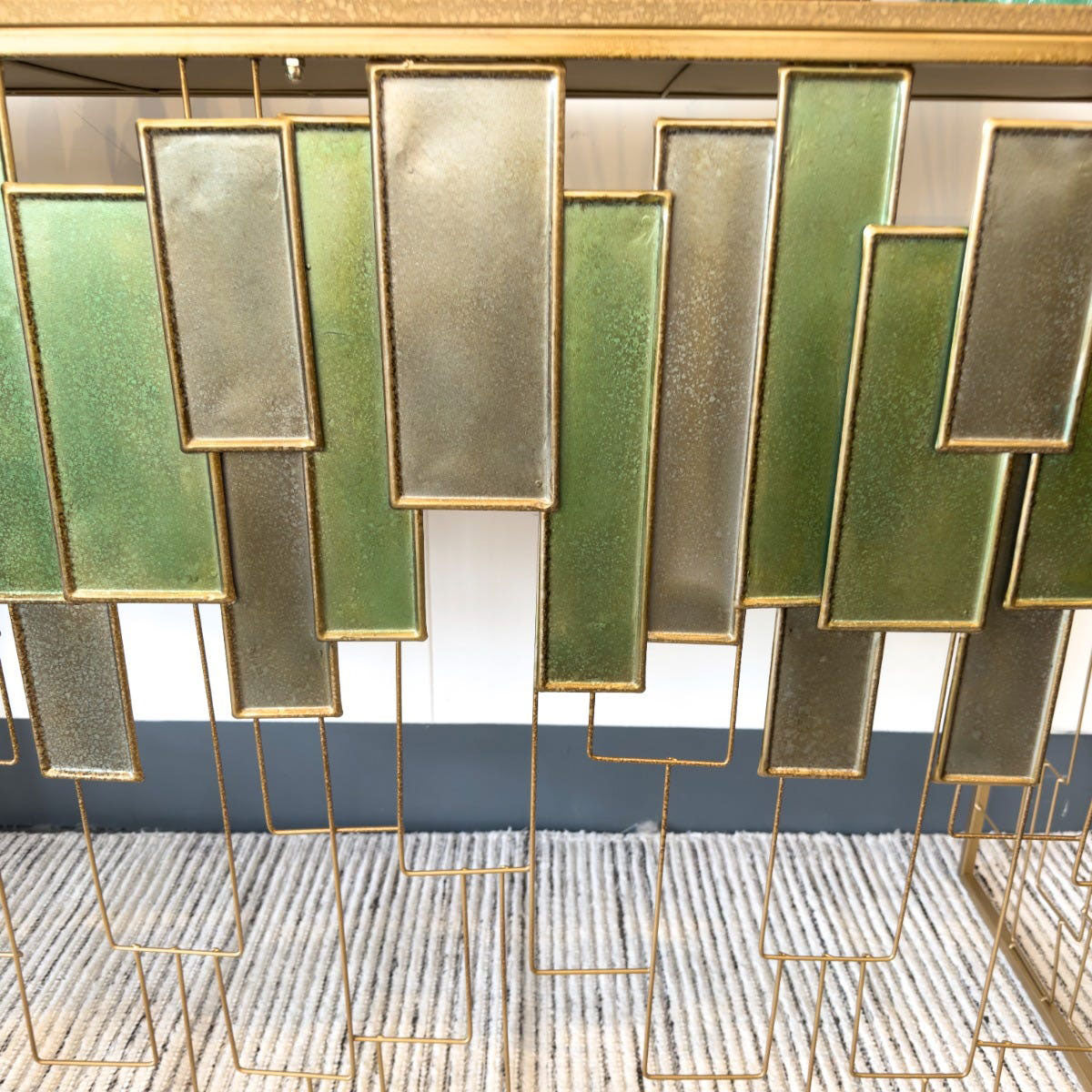 Decorative console table with green and gold rectangular panels on a white wall.
