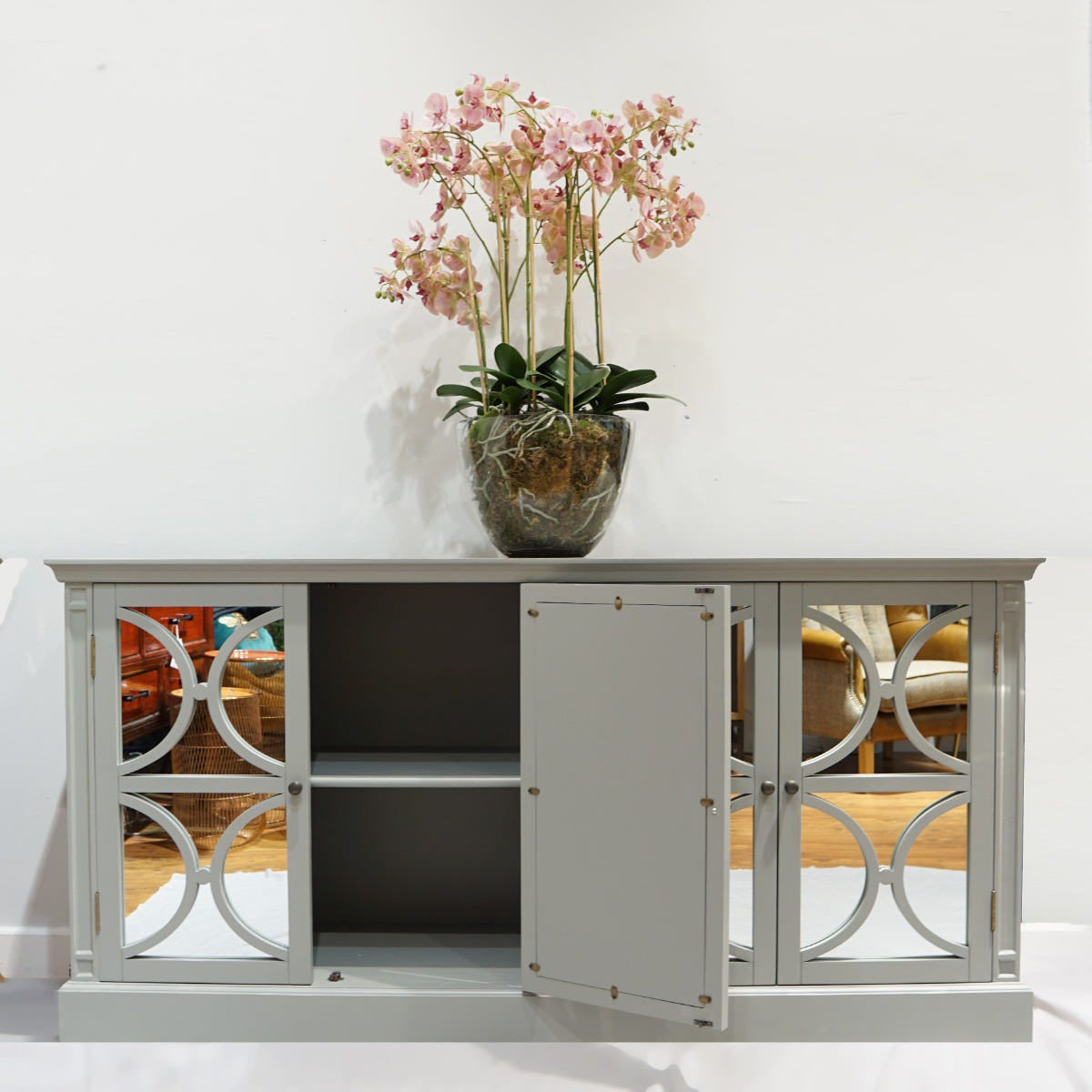 Grey mirrored sideboard with decorative glass doors and a vase of pink flowers on a white background