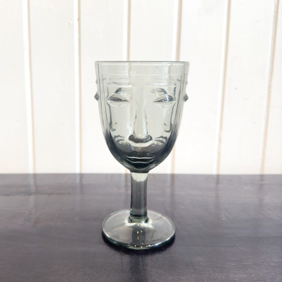 Clear glass with face design on a wooden surface and white paneled wall background