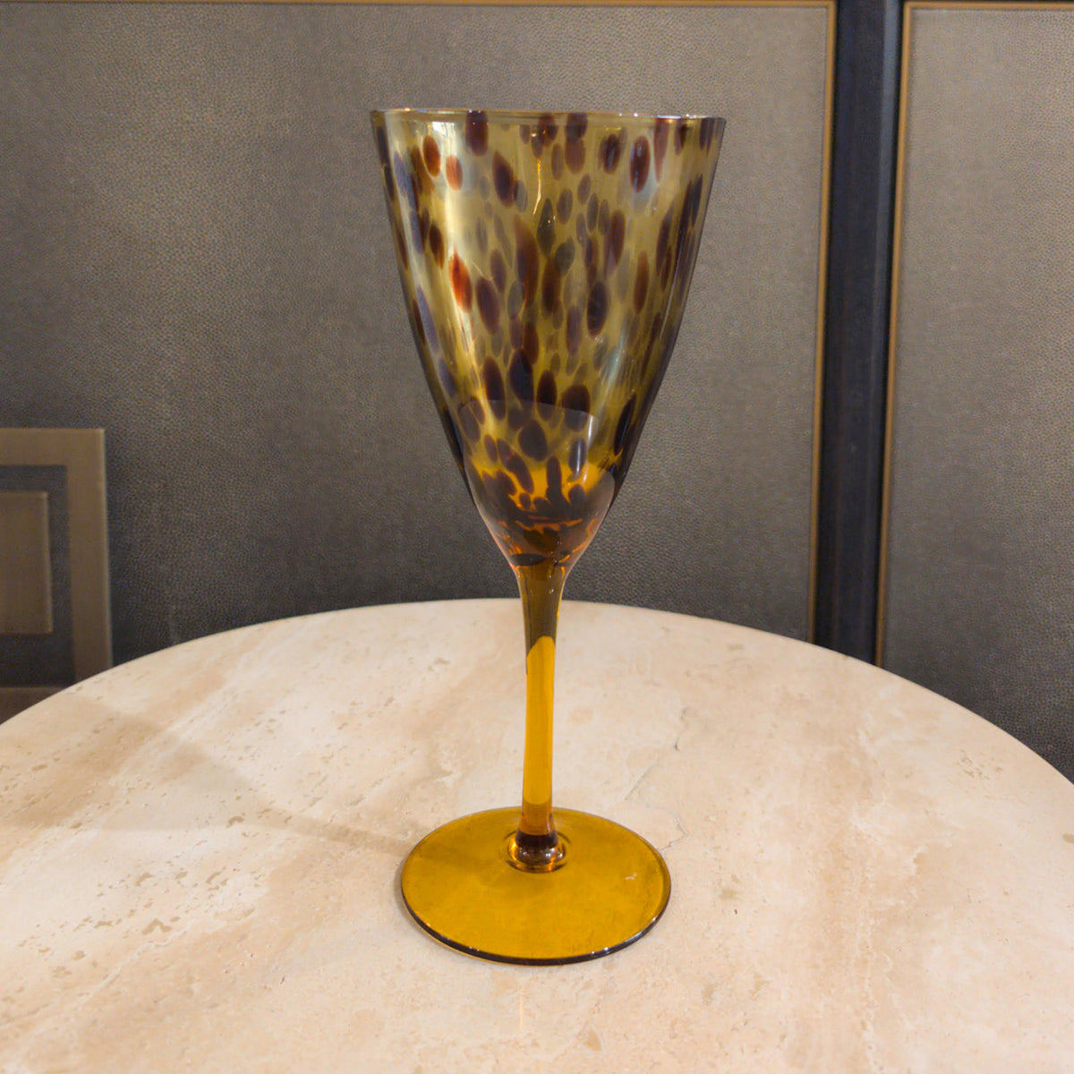 A leopard print wine glass with a gold stem and black and brown pattern, displayed on a marble surface.