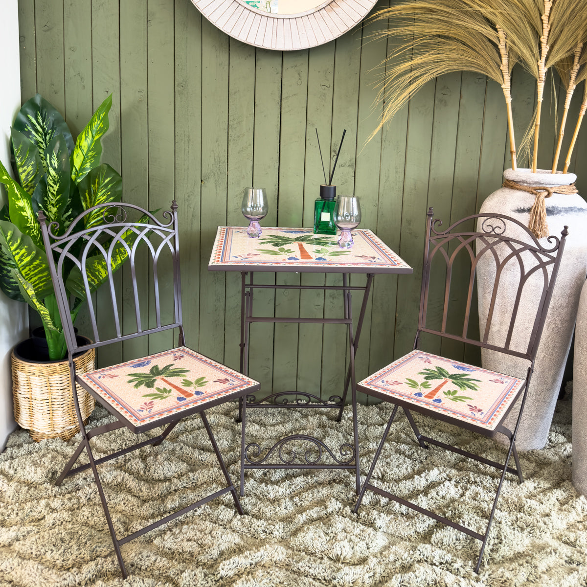 Outdoor setting with metal chairs and table against a green wall, featuring decorative elements.