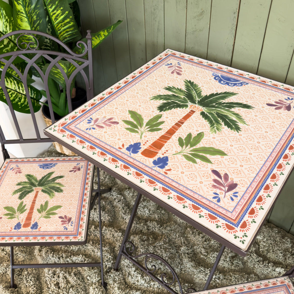Decorative outdoor table and chairs with palm tree design on a green textured rug.
