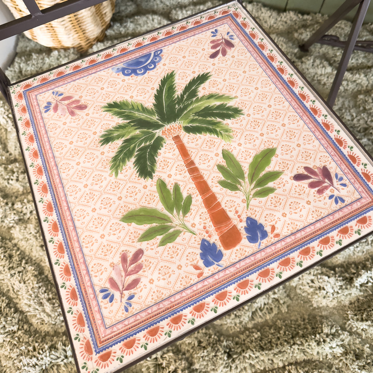 Decorative bistro chair with a palm tree design on a textured sage green rug.