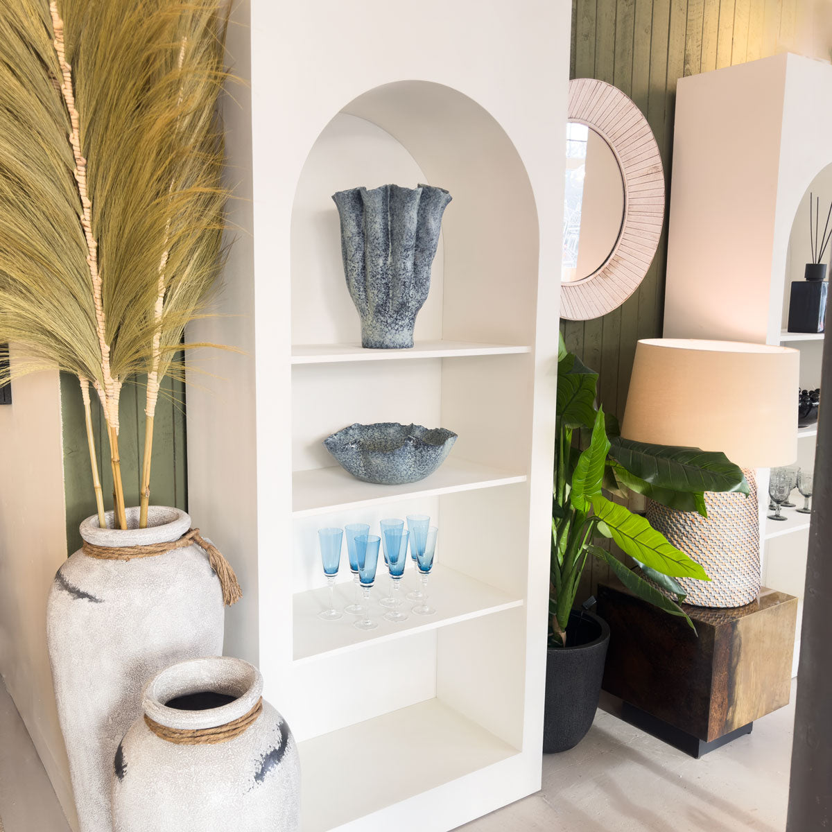 Decorative interior with white arched shelving unit, plants, and a lamp in a stylish setting.