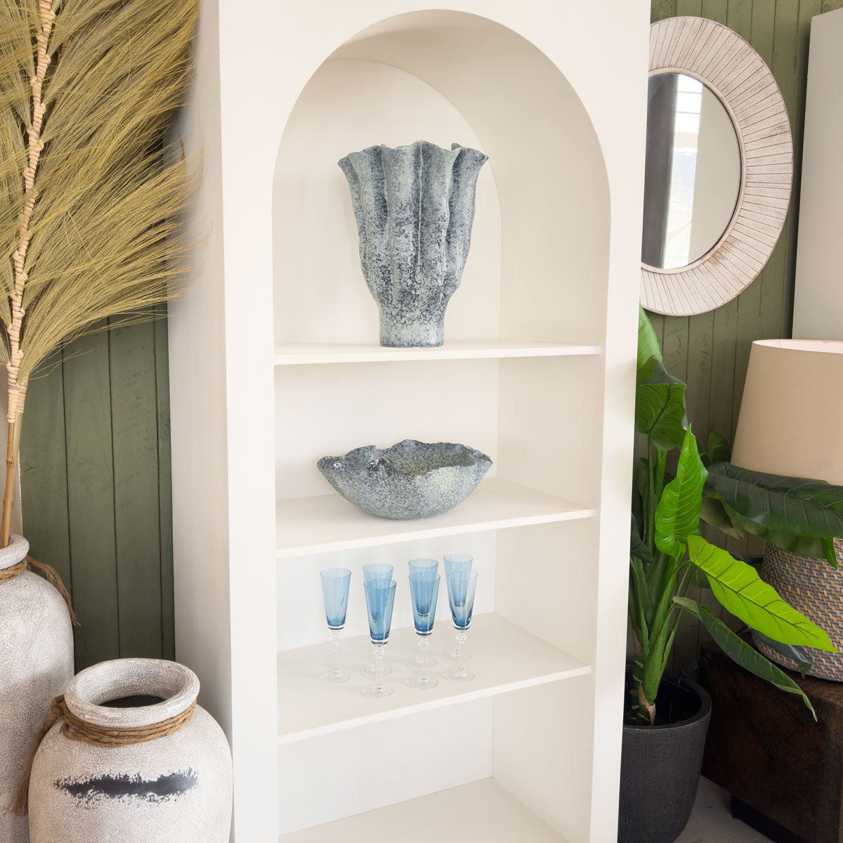 White shelving unit with decorative items in a room with green walls and plants.