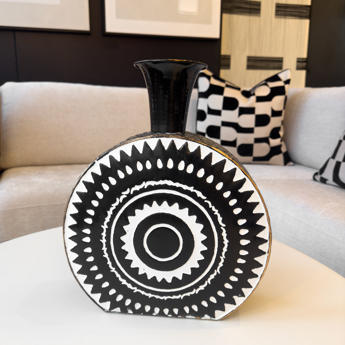 A monochrome toned circular bottle vase featuring a white aztec print, sitting on a coffee table next to a sofa.
