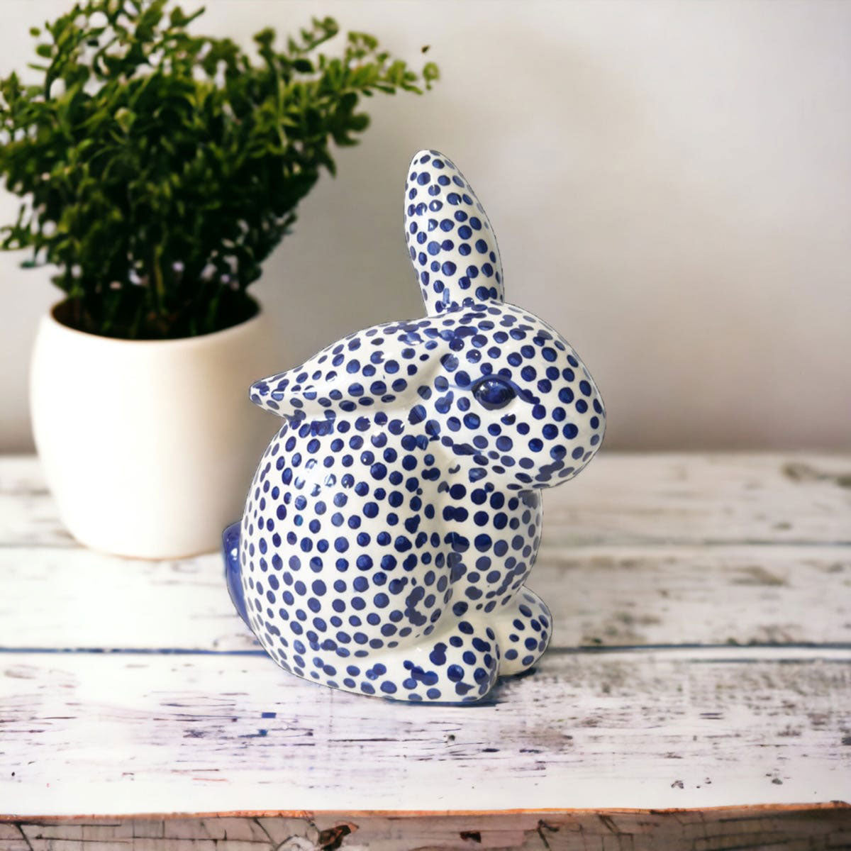 Ceramic rabbit with blue dot pattern on a wooden surface with a plant in the background