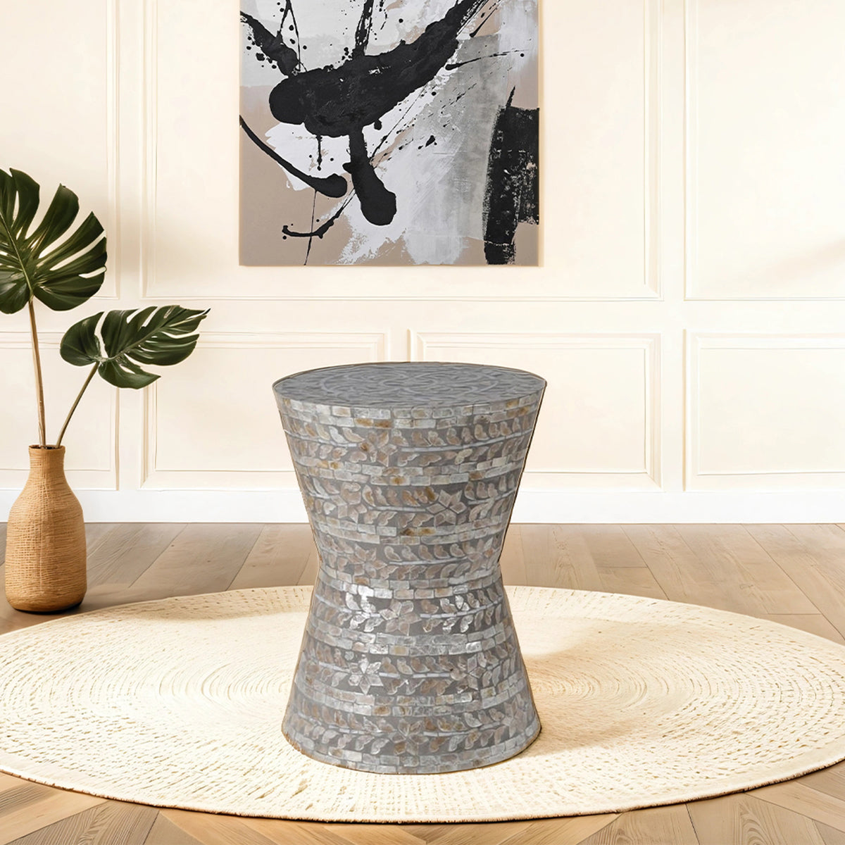 Decorative side table with a textured pattern in a room with a plant and abstract art on the wall.